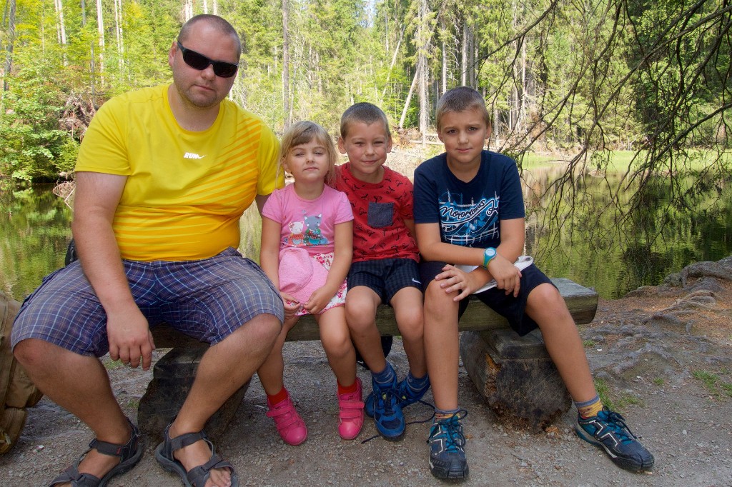 A man and three children on a log bench in front of a lake and pine forest