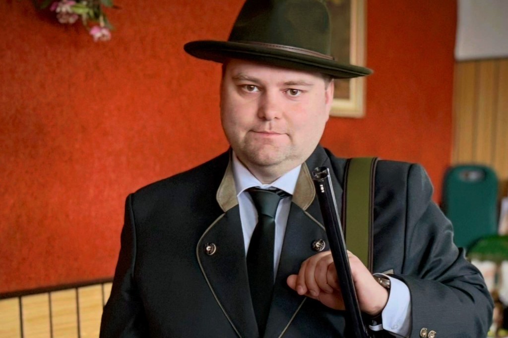 Man in traditional formal hunting attire with hat and shotgun over the shoulder