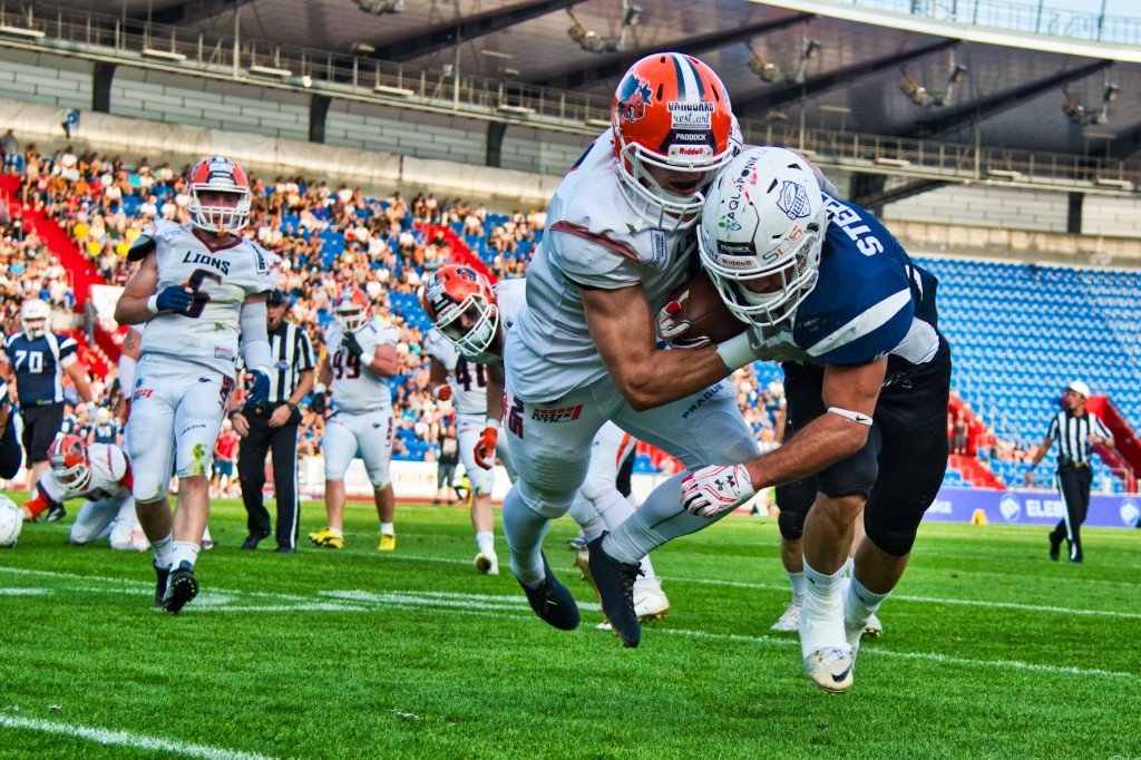 American football tackle on a green field with stadium crowd in the background