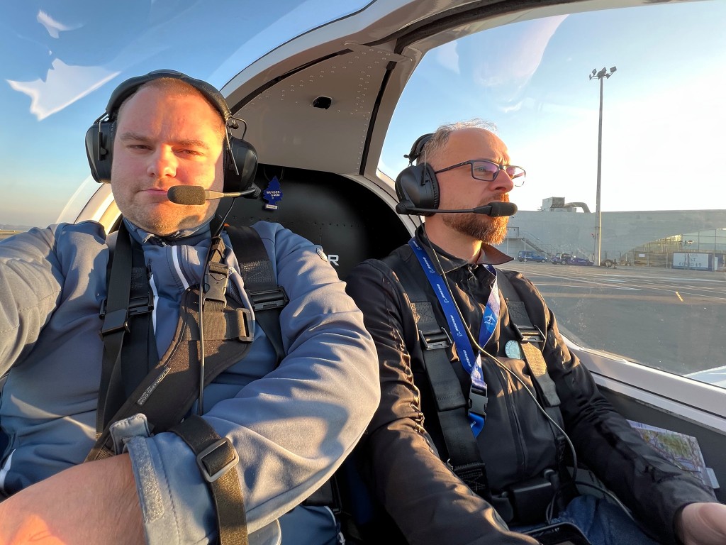 Two people in a small aircraft cockpit wearing headsets before flight