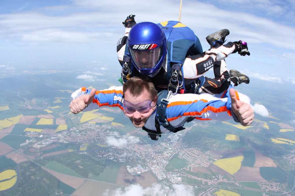 Tandem skydive with thumbs up above fields and a village below